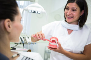 Dentist showing patient how to brush teeth in dental clinic