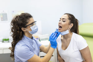 Doctor taking throat swab test from female patient. Medical worker is in protective workwear. They are at hospital during epidemic.