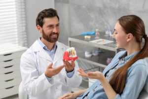 Doctor with educational model of dental implant consulting patie