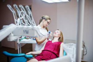Female dentist in special glasses treating her patient’s teeth w
