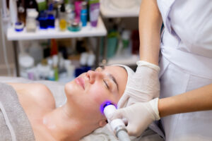 A young beautiful girl lies on the beautician’s table and receives procedures with a professional apparatus for skin rejuvenation and moisturizing